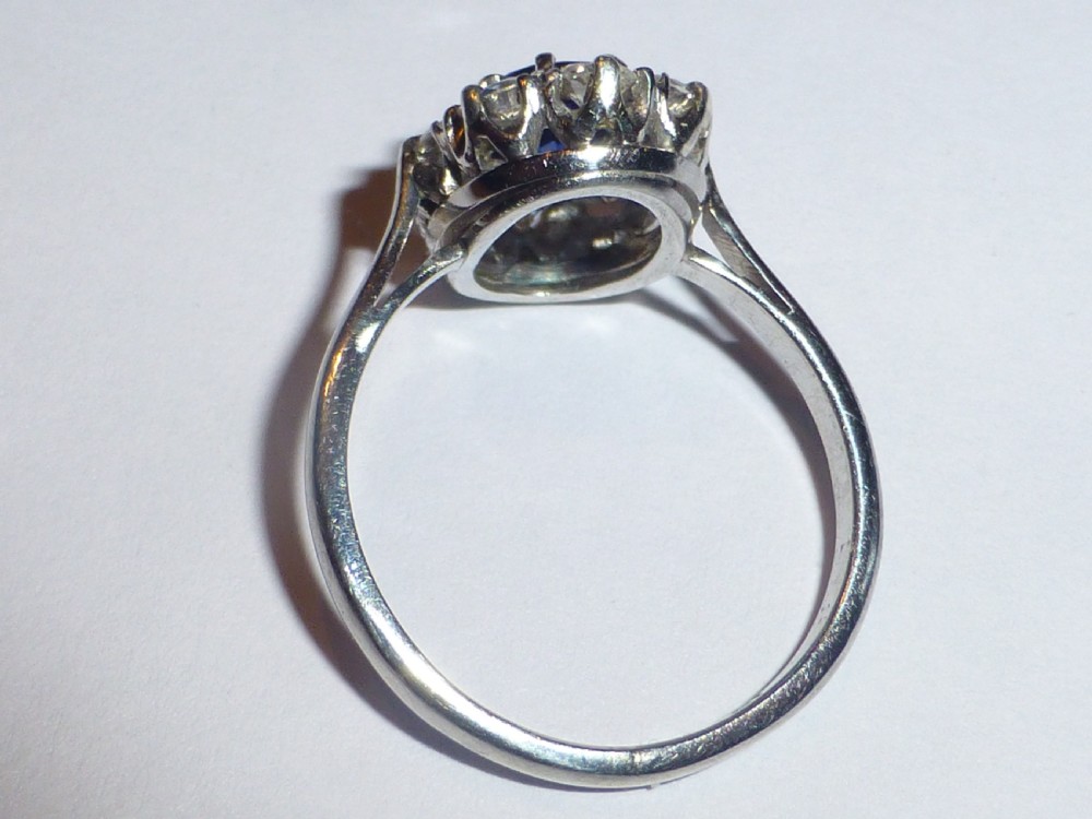 An Art Deco platinum cluster ring featuring a central oval blue sapphire surrounded by a halo of round diamonds. View IV