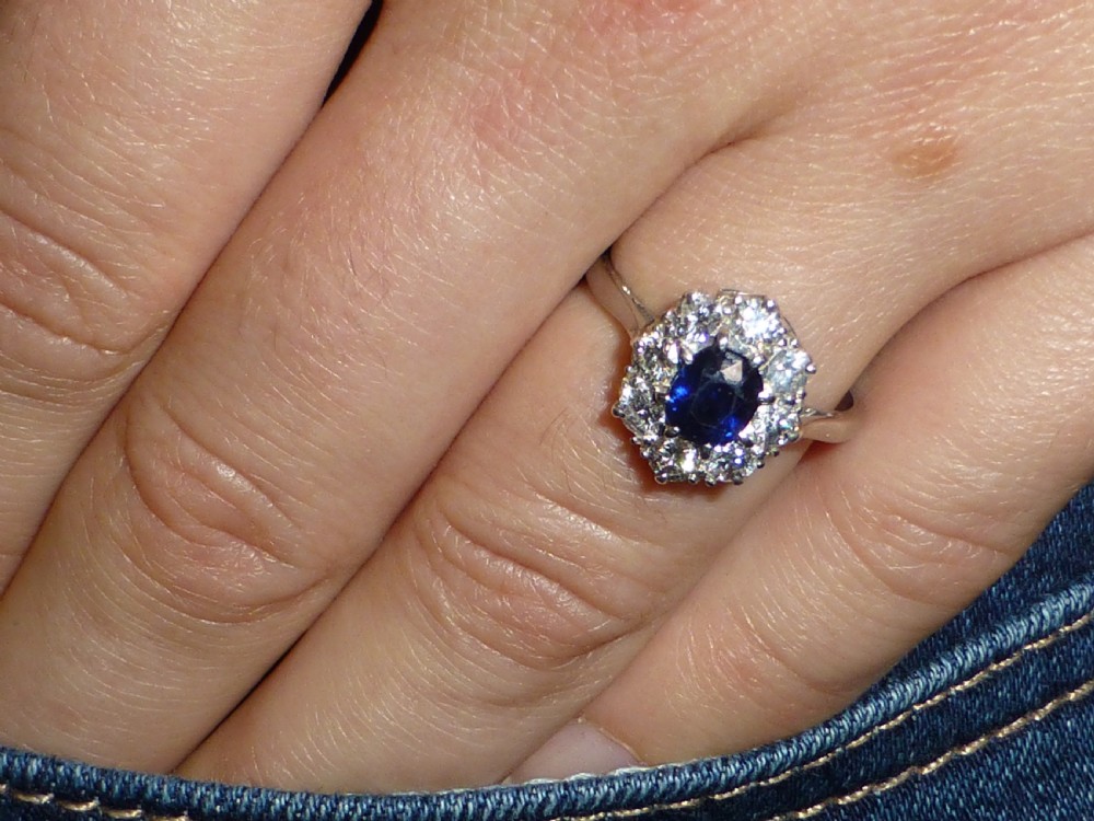 An Art Deco platinum cluster ring featuring a central oval blue sapphire surrounded by a halo of round diamonds. View VI