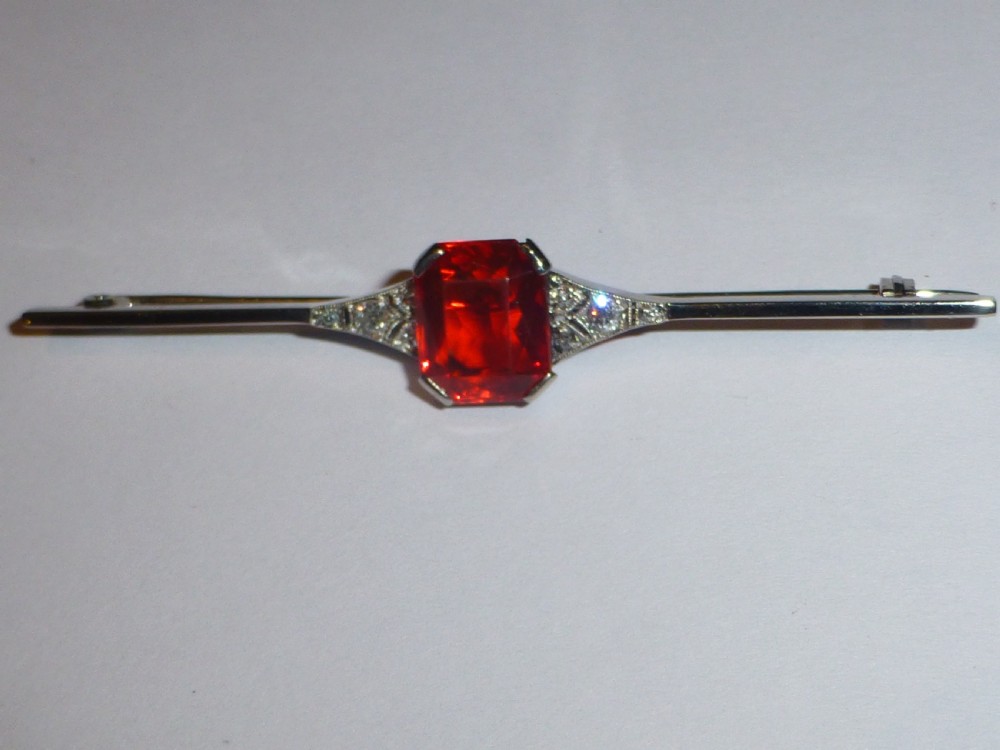 An Edwardian 18ct white gold bar brooch featuring a central emerald-cut orange fire opal flanked by diamond accents. View III