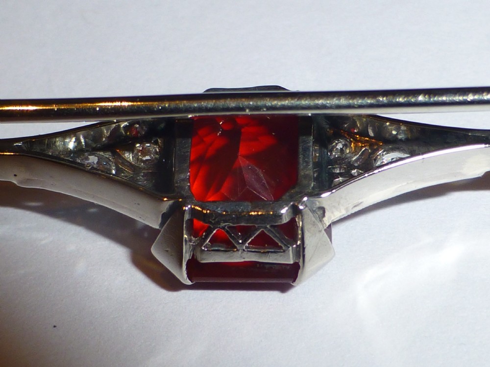 An Edwardian 18ct white gold bar brooch featuring a central emerald-cut orange fire opal flanked by diamond accents. View VI