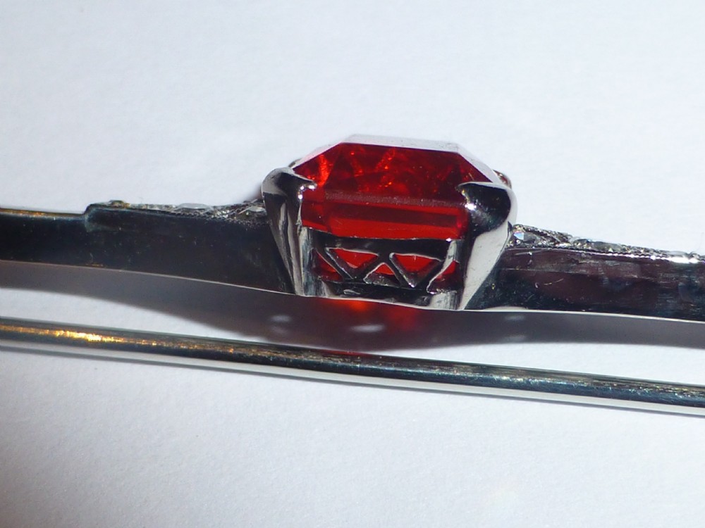 An Edwardian 18ct white gold bar brooch featuring a central emerald-cut orange fire opal flanked by diamond accents. View VII