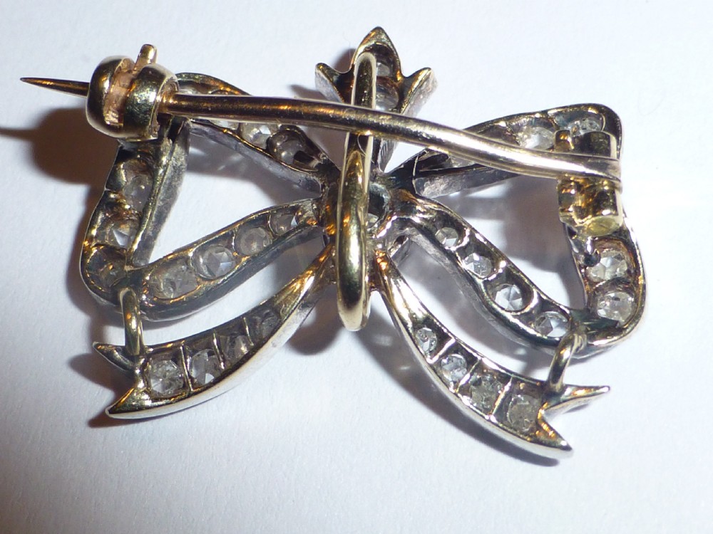 A nineteenth-century bow-shaped brooch set with diamonds in silver-topped gold, featuring a central round diamond and a pin fitting on the reverse. View V
