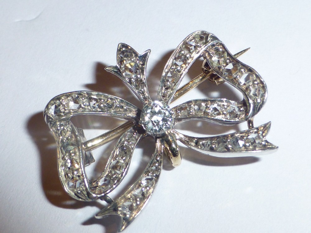 A nineteenth-century bow-shaped brooch set with diamonds in silver-topped gold, featuring a central round diamond and a pin fitting on the reverse. View XI