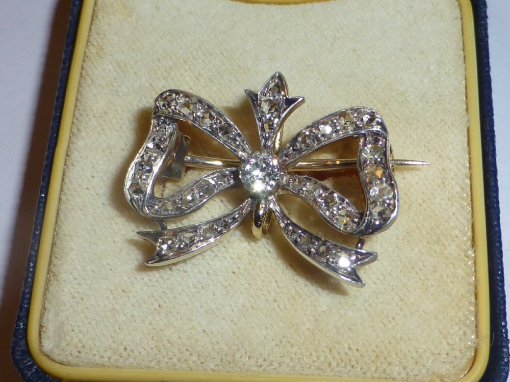 A nineteenth-century bow-shaped brooch set with diamonds in silver-topped gold, featuring a central round diamond and a pin fitting on the reverse. View XVII