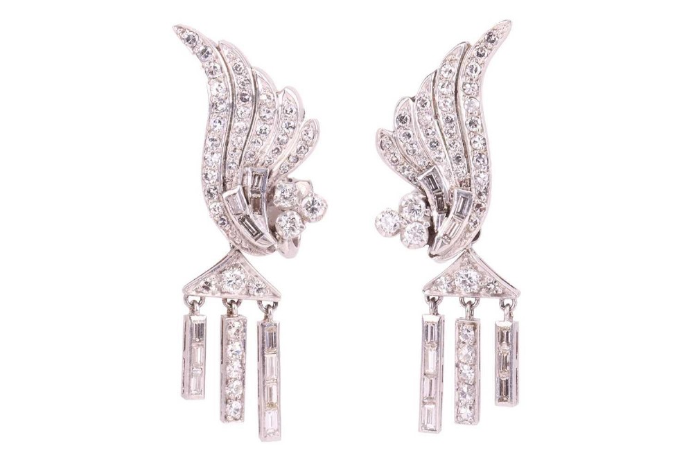 A pair of Art Deco platinum earrings set with round and baguette diamonds, featuring winged tops and detachable geometric drop pendants.