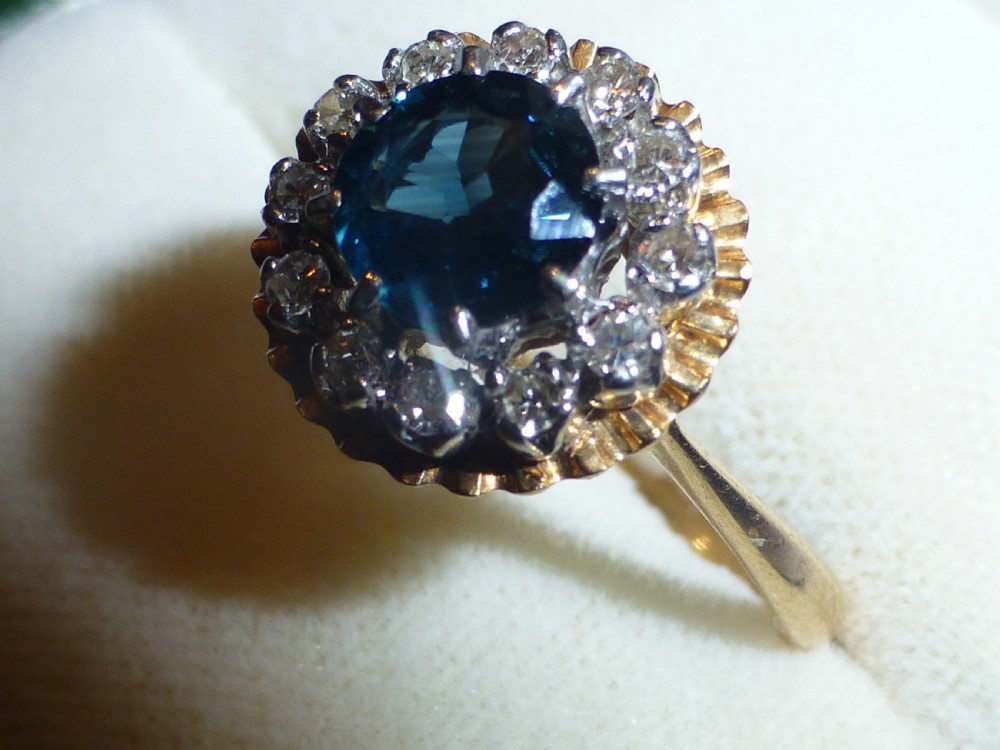 An antique gold ring featuring a central round deep blue sapphire framed by a halo of small diamonds within a scalloped edge setting. View III