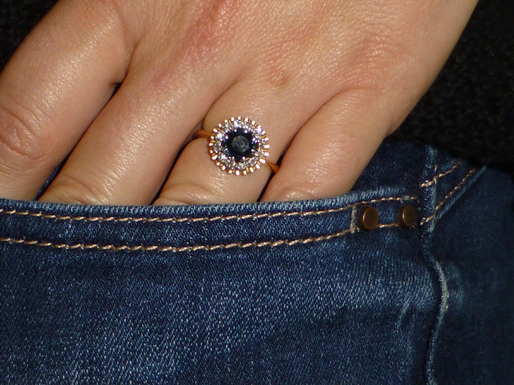 An antique gold ring featuring a central round deep blue sapphire framed by a halo of small diamonds within a scalloped edge setting. View VI
