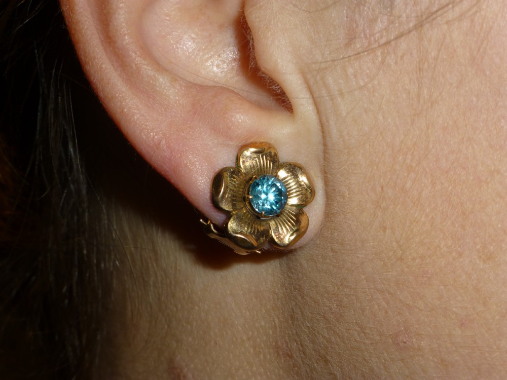 A pair of gold flower-shaped earrings, each featuring a round blue zircon gemstone held in a central claw setting. View II