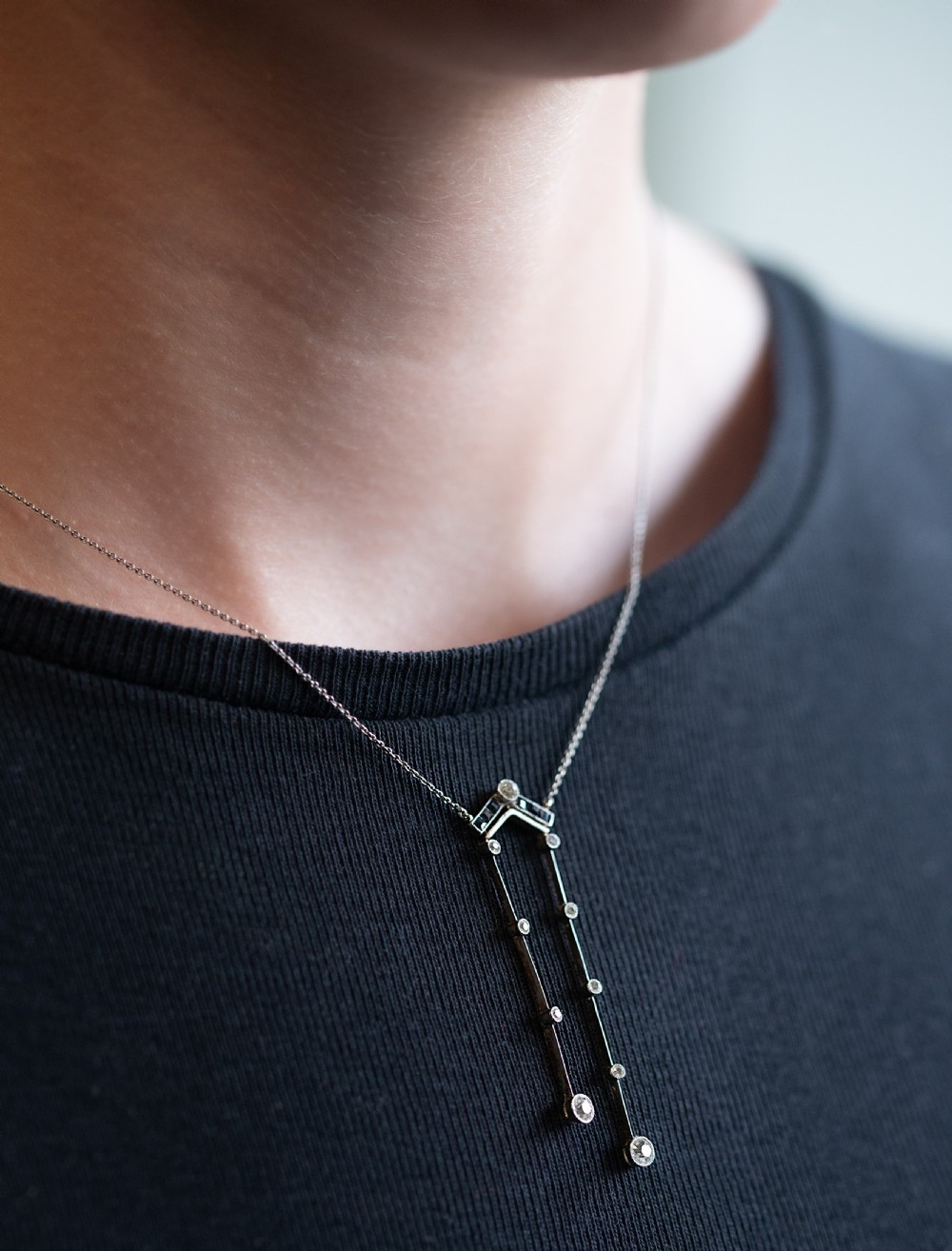 An Edwardian platinum pendant necklace featuring a chevron bar set with sapphires and two vertical diamond drops of unequal length suspended on a fine chain.
