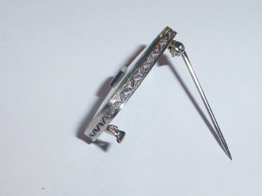 An Art Deco rectangular white gold brooch featuring a starburst-carved translucent rock crystal quartz plaque set with a central diamond, surrounded by green chrysoprase and black onyx inlays. View IV