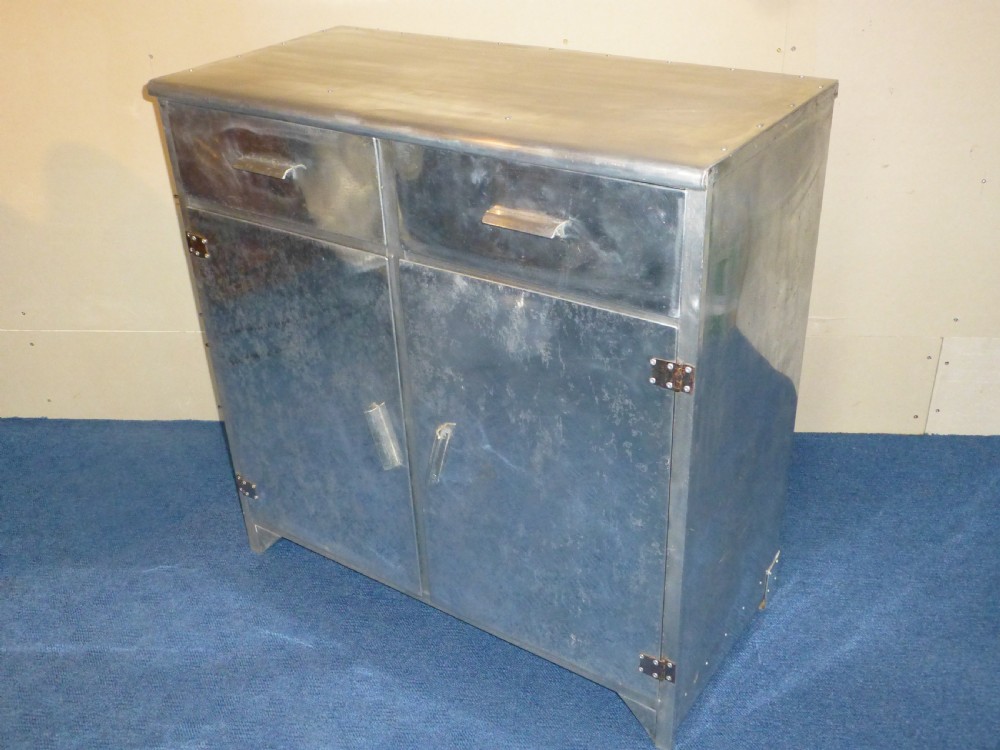 An aluminium metal sideboard featuring two upper drawers, two lower cabinet doors, riveted joinery, and exposed metal hinges.