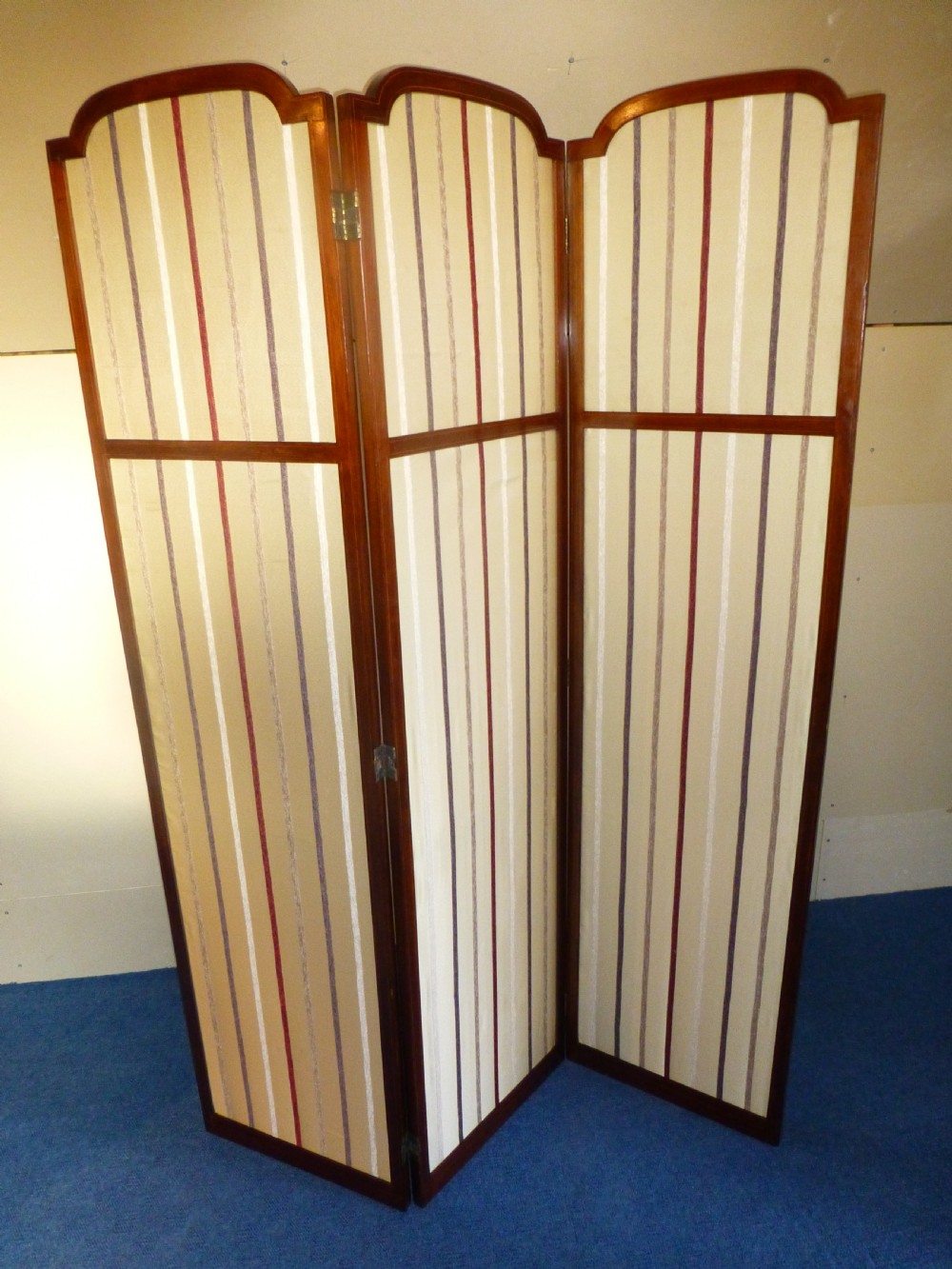 An Edwardian three-panel mahogany folding screen featuring arched top rails and cream striped fabric inserts.