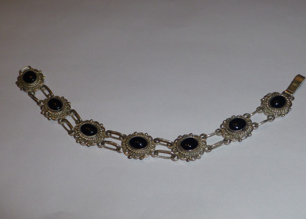 A silver link bracelet featuring oval black onyx cabochons held within pierced filigree frames.