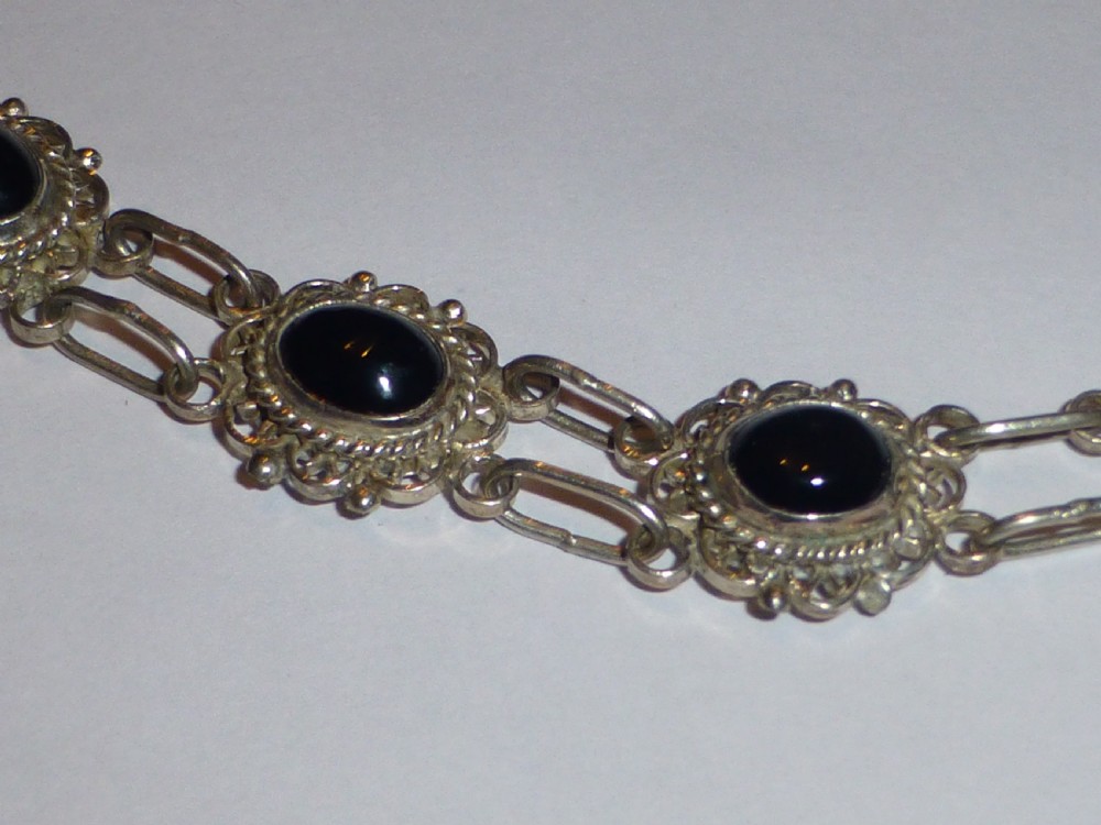 A silver link bracelet featuring oval black onyx cabochons held within pierced filigree frames. View III