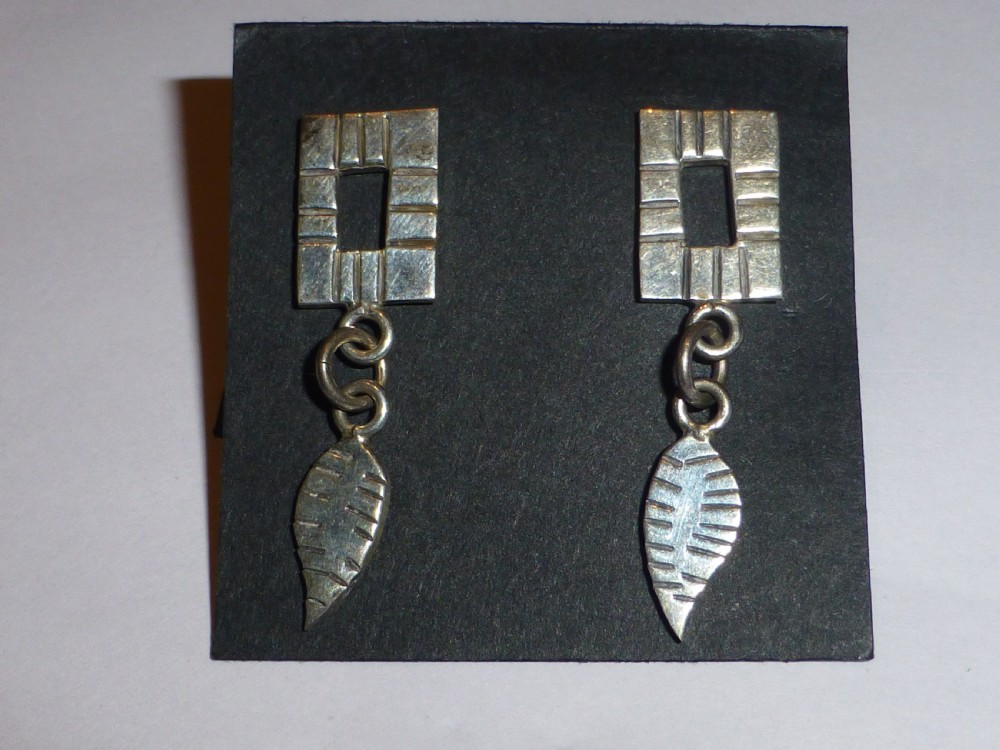 A pair of silver drop earrings featuring open rectangular textured tops connected by double jump rings to leaf-shaped pendants.