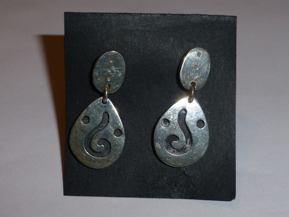 A pair of silver drop earrings featuring oval tops and teardrop-shaped pendants adorned with scroll cutouts and small circular indentations.