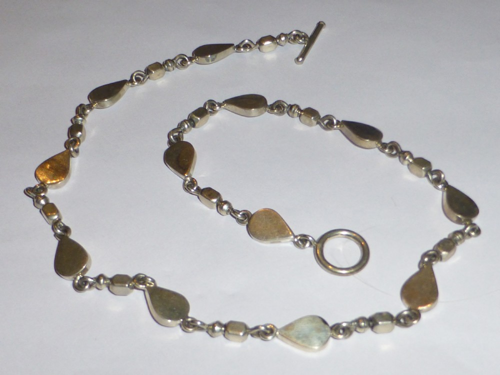 A vintage sterling silver link necklace featuring repeating teardrop motifs and small silver bead spacers secured with a toggle clasp.