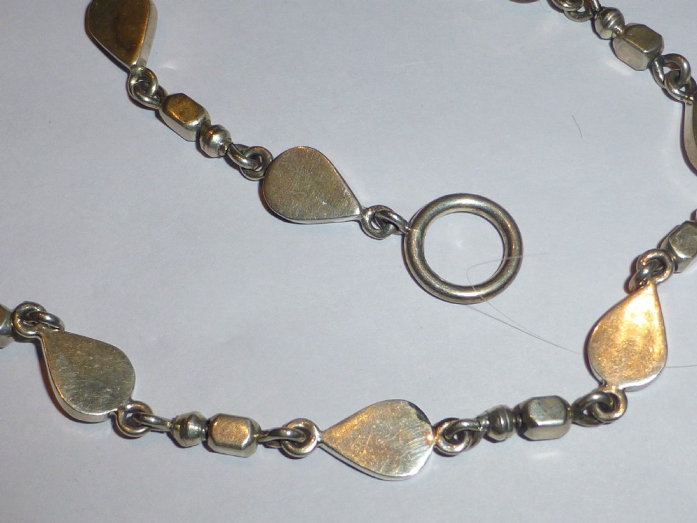 A vintage sterling silver link necklace featuring repeating teardrop motifs and small silver bead spacers secured with a toggle clasp. View IV