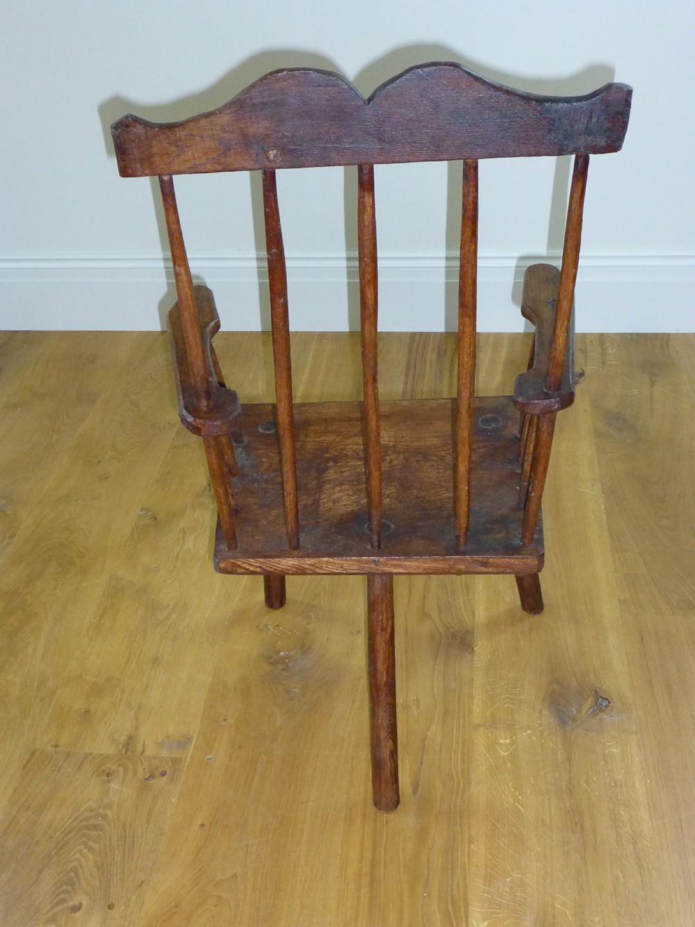 A primitive dark brown wooden Welsh stick armchair featuring a comb back crest rail, hand-shaped spindles, flat armrests, and a solid slab seat on splayed legs. View III
