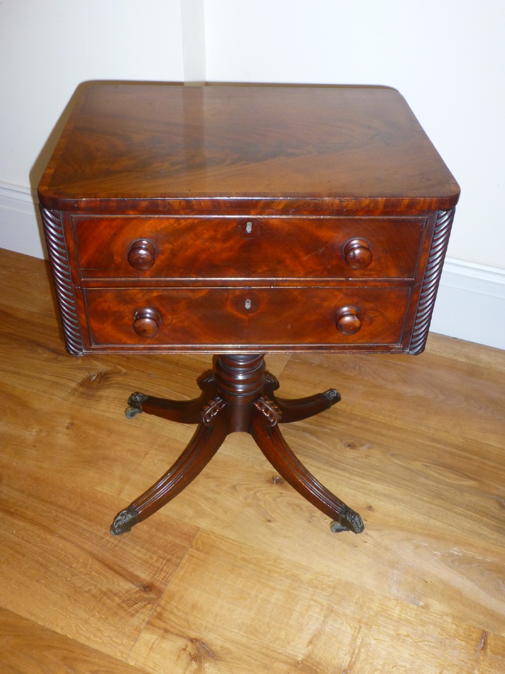 A Regency mahogany work table featuring two drawers with wooden knobs, spirally reeded side columns, and a turned pedestal base on quadruped sabre legs with brass castors.