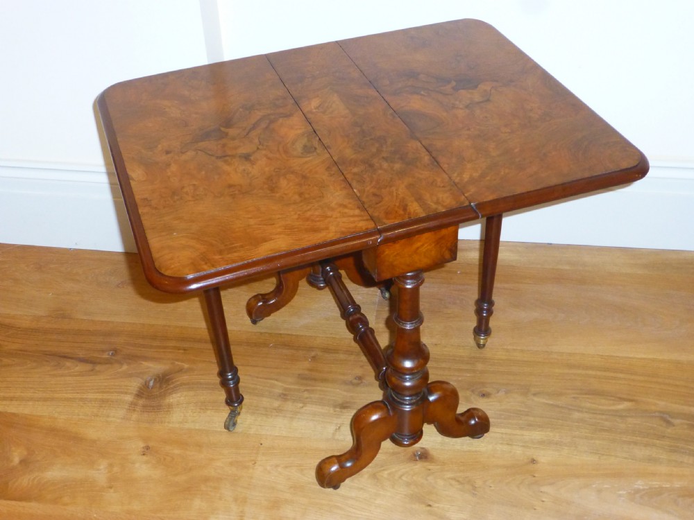 A Victorian burr walnut Sutherland table featuring two drop leaves, turned supports, carved trestle feet, and brass castors.