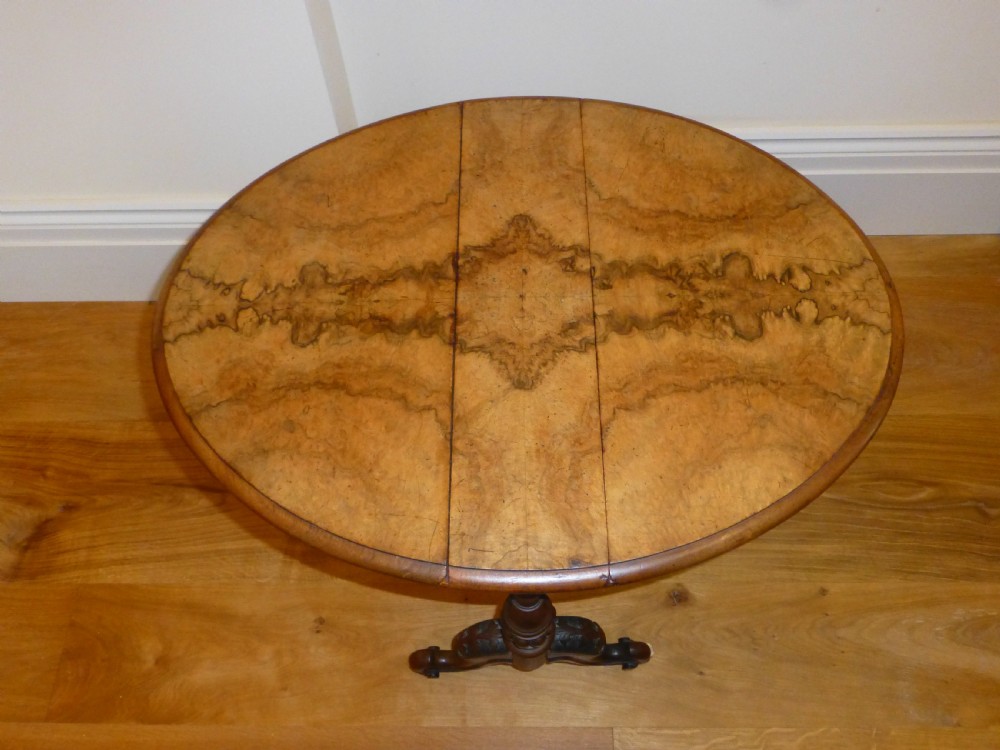 A Victorian burr walnut Sutherland table featuring drop-leaf sides, turned twin supports, and carved legs resting on white ceramic castors. View II