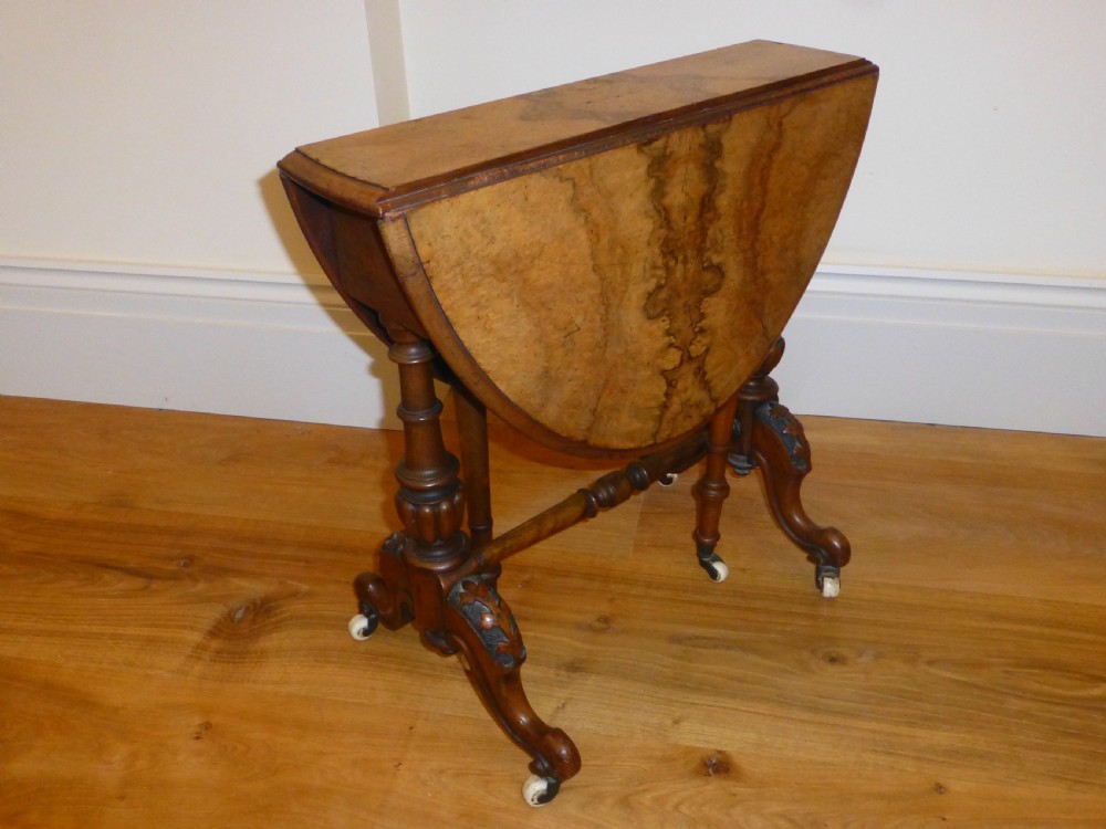 A Victorian burr walnut Sutherland table featuring drop-leaf sides, turned twin supports, and carved legs resting on white ceramic castors. View III