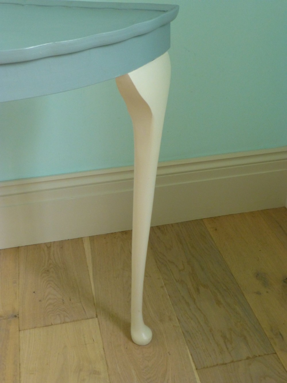 A painted demi lune console table featuring a light blue top surface and cream three-legged base with slender pad feet. View II