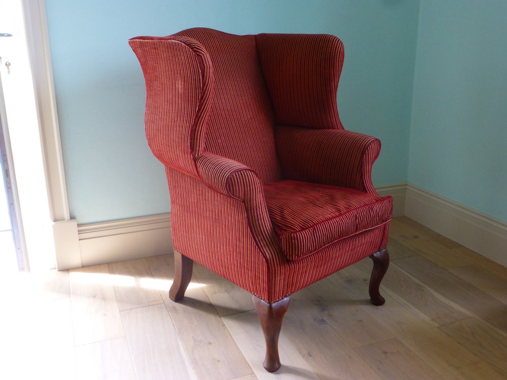 An 18th-century Georgian wingback armchair upholstered in red and gold striped fabric with carved cabriole front legs.