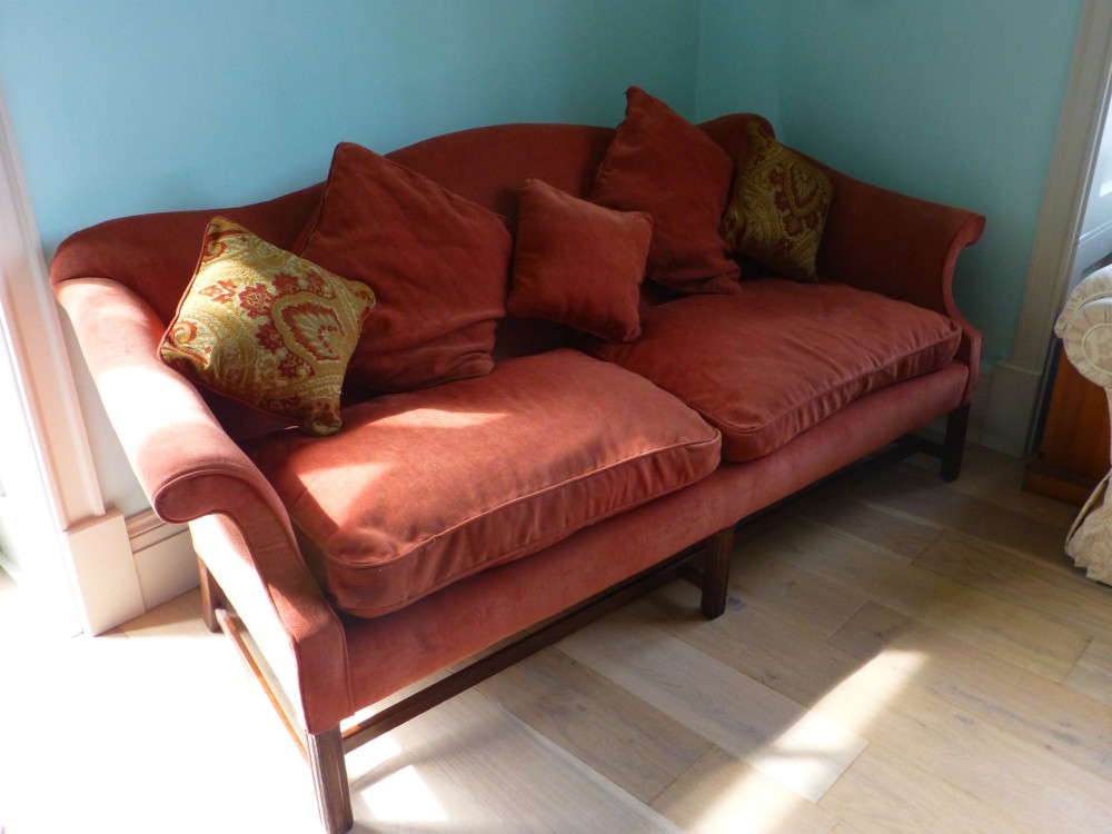 A 19th-century serpentine camel back sofa upholstered in terracotta fabric with mahogany straight legs and stretchers.