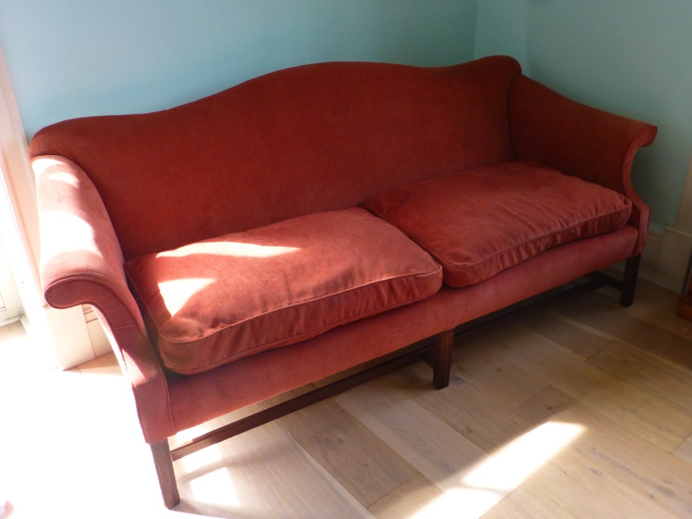 A 19th-century serpentine camel back sofa upholstered in terracotta fabric with mahogany straight legs and stretchers. View IV