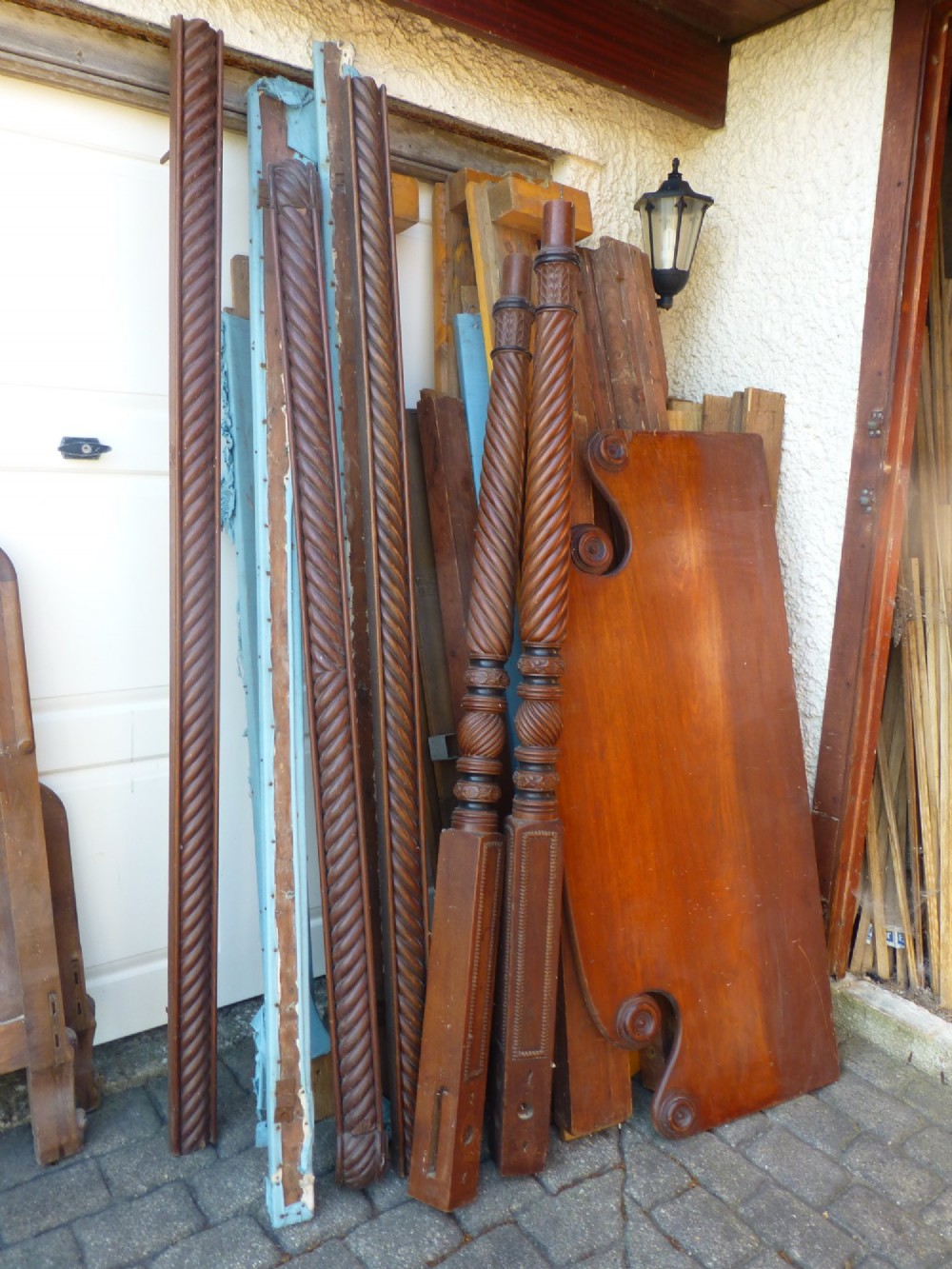 Dismantled components of a wooden four poster bed, including spiral-carved posts, reeded rails, and a shaped mahogany headboard.