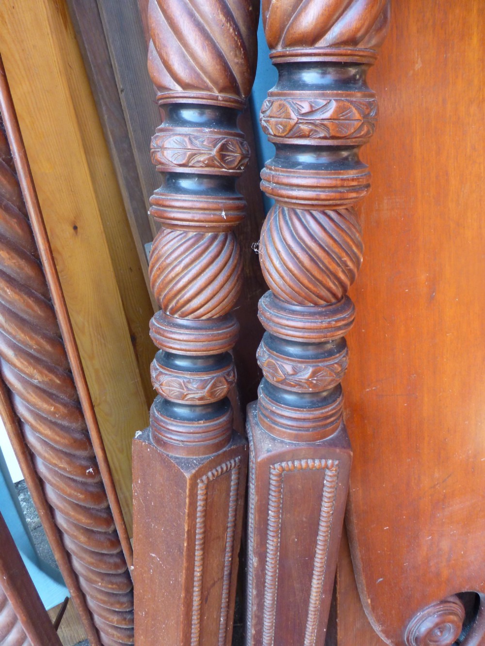 Dismantled components of a wooden four poster bed, including spiral-carved posts, reeded rails, and a shaped mahogany headboard. View III