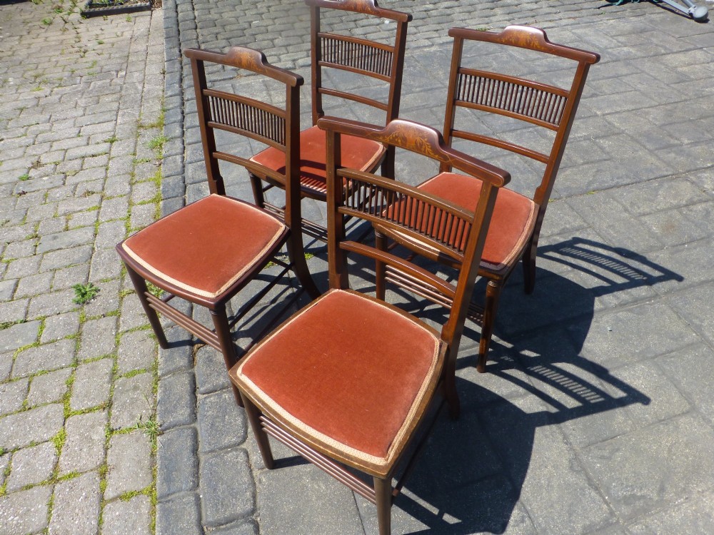 A set of four dark mahogany Edwardian dining chairs featuring decorative crest rail inlay and terracotta velvet seats.