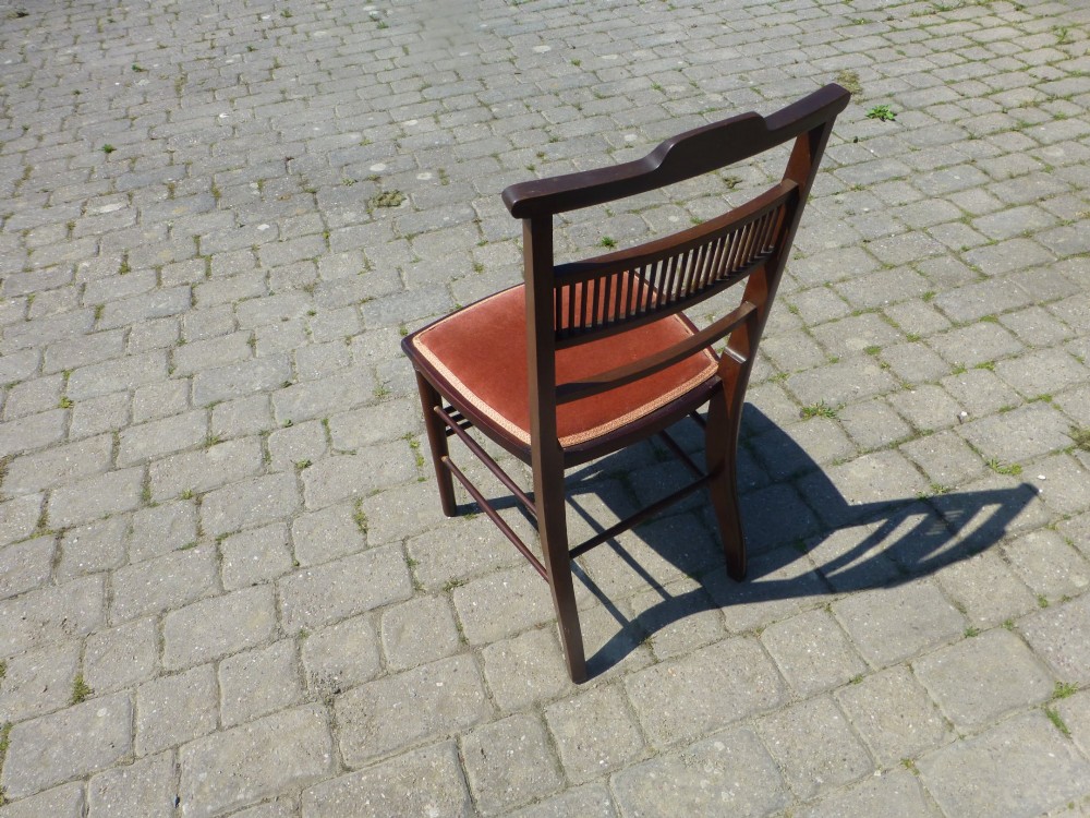 A set of four dark mahogany Edwardian dining chairs featuring decorative crest rail inlay and terracotta velvet seats. View V