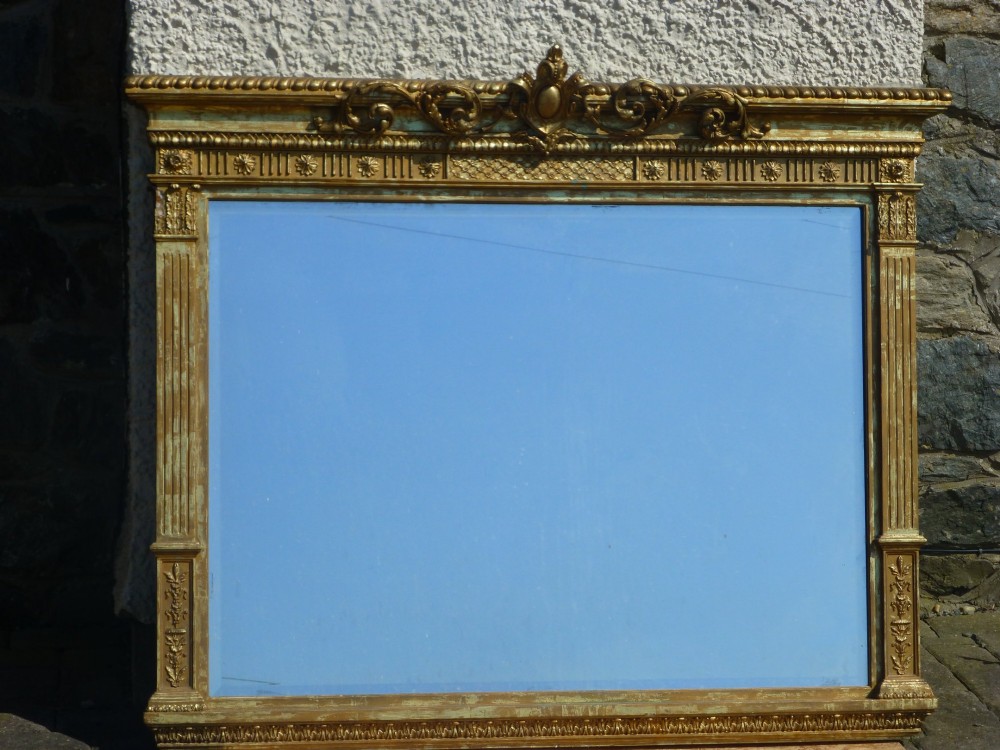 A large rectangular nineteenth-century gilt overmantel mirror featuring fluted pilasters, rosette corner embellishments, and a central leaf cresting.
