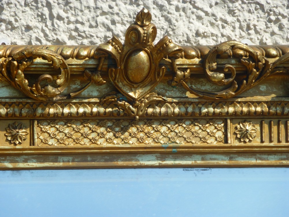 A large rectangular nineteenth-century gilt overmantel mirror featuring fluted pilasters, rosette corner embellishments, and a central leaf cresting. View II