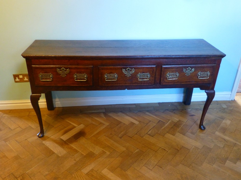 An 18th-century dark oak Georgian dresser base featuring three drawers with pierced brass handles and front cabriole legs. View II