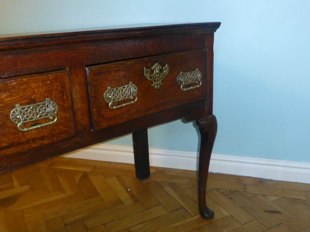 An 18th-century dark oak Georgian dresser base featuring three drawers with pierced brass handles and front cabriole legs. View IV