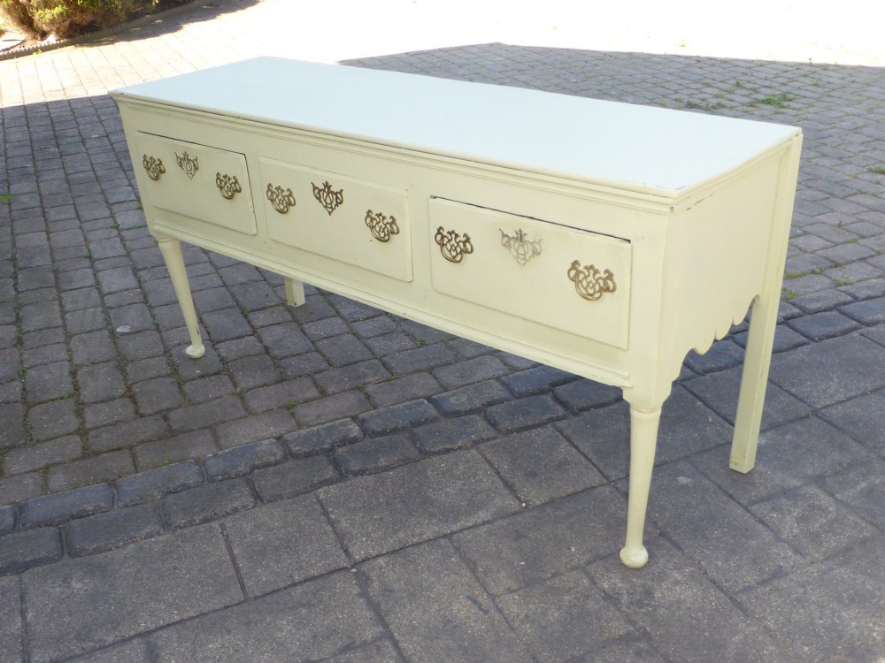 An 18th-century Georgian painted oak dresser base featuring three drawers with decorative brass handles, supported by slender legs with shaped side aprons.