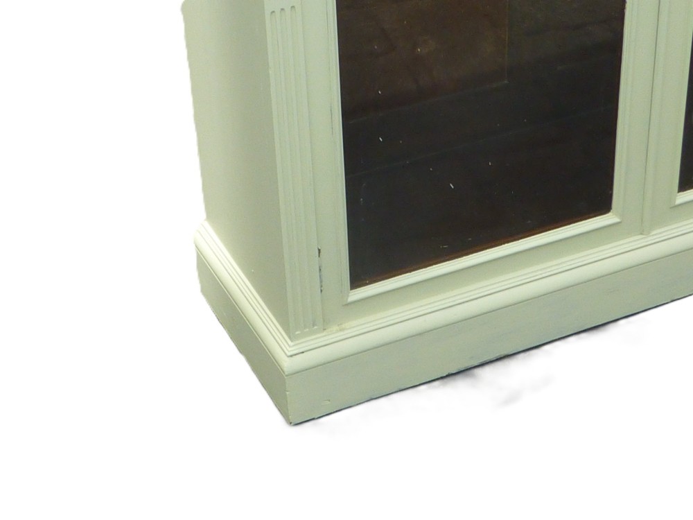 A 19th-century off-white painted bookcase featuring three glazed glass doors, fluted side pilasters, and a contrasting dark interior. View II