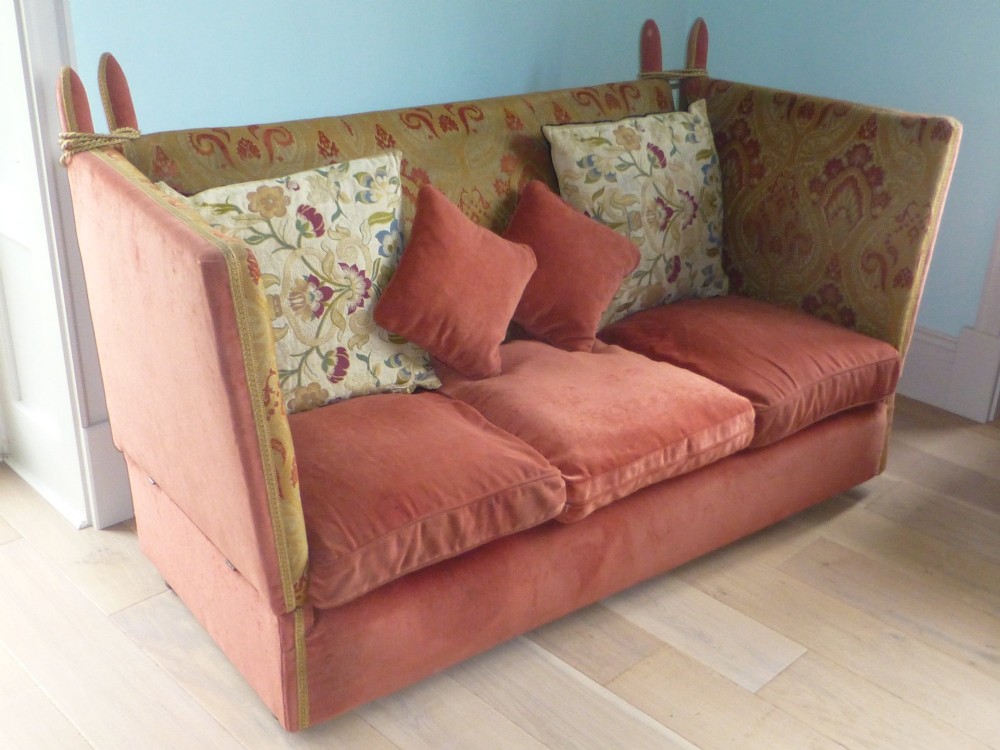 A nineteenth-century Victorian Knole sofa upholstered in terracotta velvet with patterned woven fabric lining, featuring high adjustable sides attached to carved corner finials with cords.