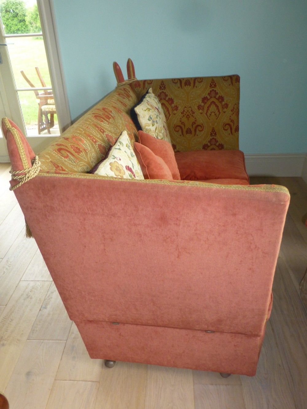 A nineteenth-century Victorian Knole sofa upholstered in terracotta velvet with patterned woven fabric lining, featuring high adjustable sides attached to carved corner finials with cords. View IV