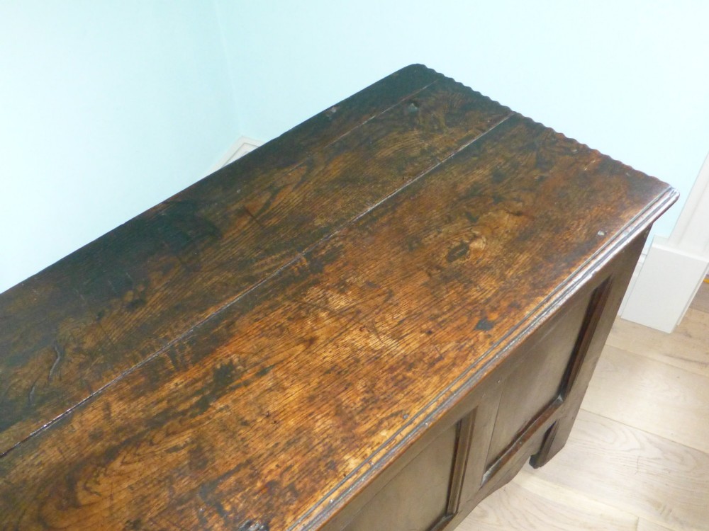 A dark oak 17th-century Welsh coffer featuring a four-panel front, hinged top lid, shaped lower apron, and integrated stile feet. View II