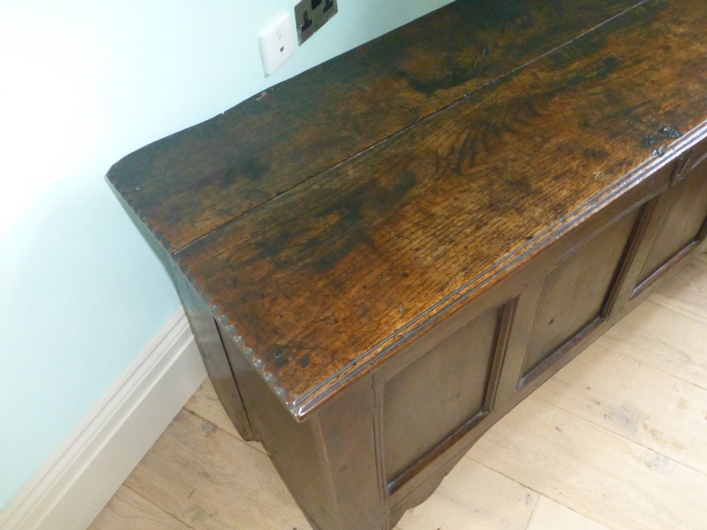 A dark oak 17th-century Welsh coffer featuring a four-panel front, hinged top lid, shaped lower apron, and integrated stile feet. View III
