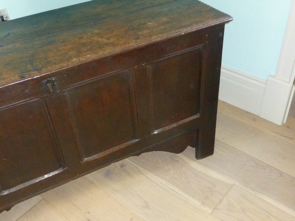 A dark oak 17th-century Welsh coffer featuring a four-panel front, hinged top lid, shaped lower apron, and integrated stile feet. View IV