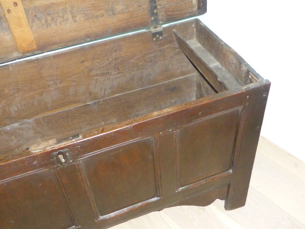 A dark oak 17th-century Welsh coffer featuring a four-panel front, hinged top lid, shaped lower apron, and integrated stile feet. View V