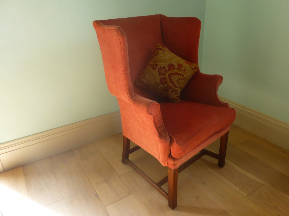 A 19th-century wingback armchair upholstered in terracotta fabric with dark mahogany legs and stretchers.