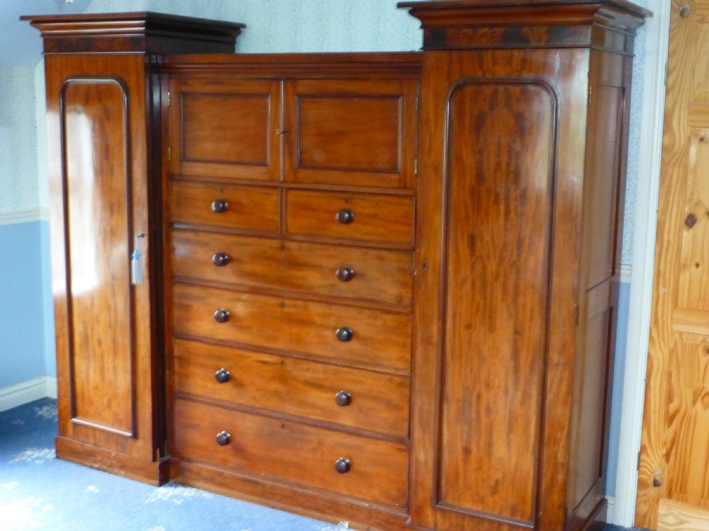 A nineteenth-century mahogany inverted breakfront compactum wardrobe featuring a central chest of drawers beneath small double cupboards, flanked by two tall panelled side wings.
