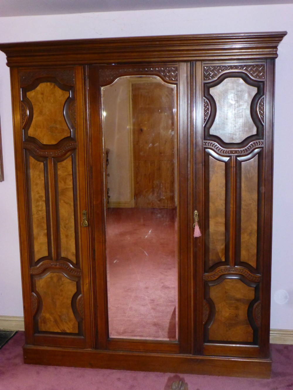 A mid-19th-century Victorian triple wardrobe made of rich burr walnut, featuring a central full-length mirror door flanked by two carved panelled doors.